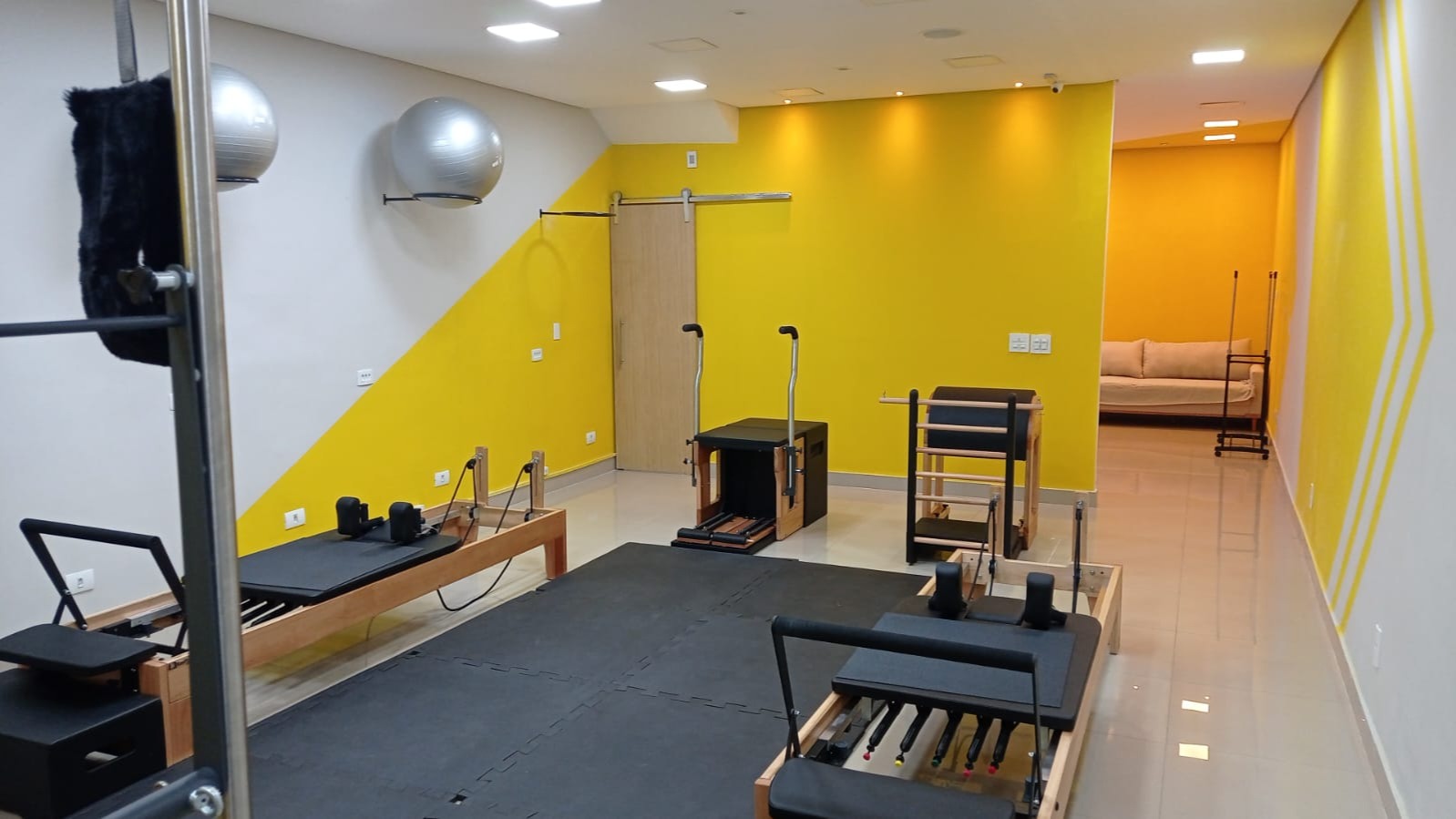 Sala de pilates no Tatuapé com reformers, cadeira, barrel e parede amarela em diagonal